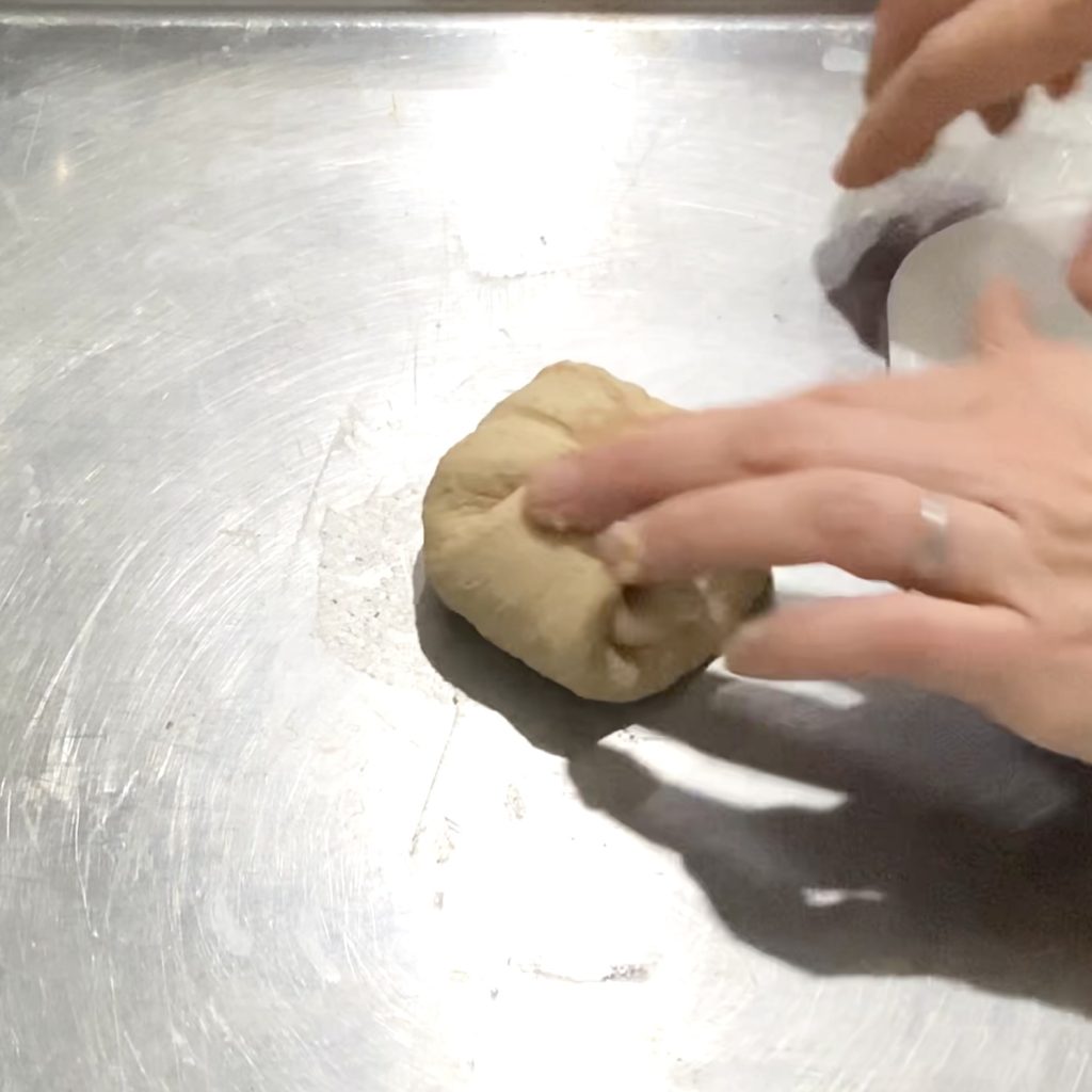 Pressing dough down into the center to shape a ball